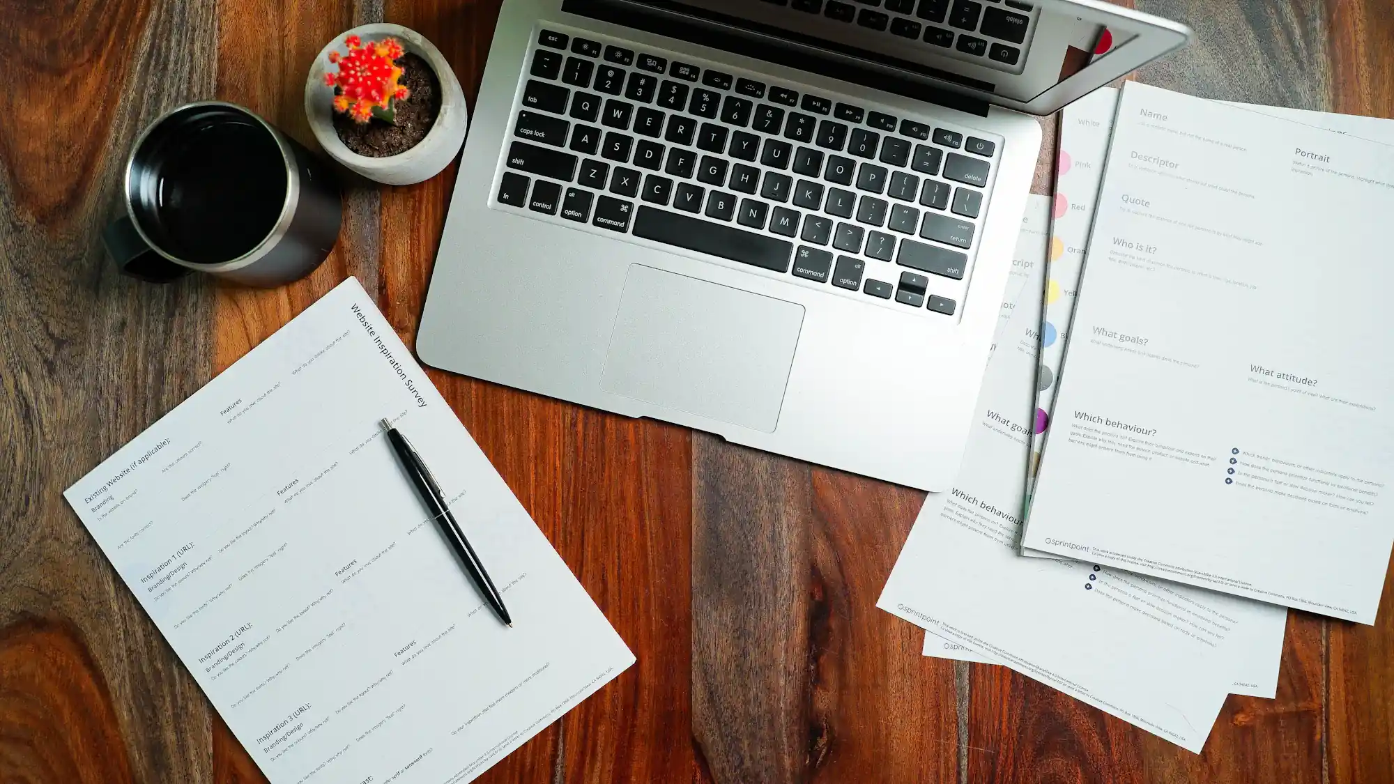 A laptop, notes and a cup of coffee on a wooden desk, seen from above