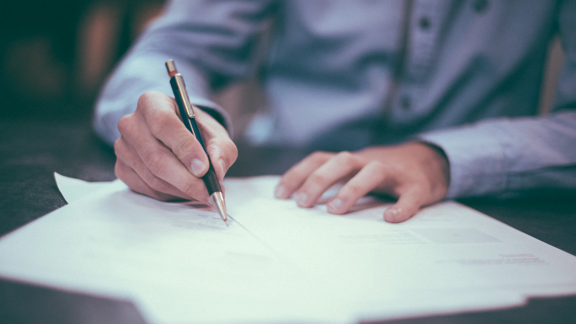 A hand signing a printed document on a desk