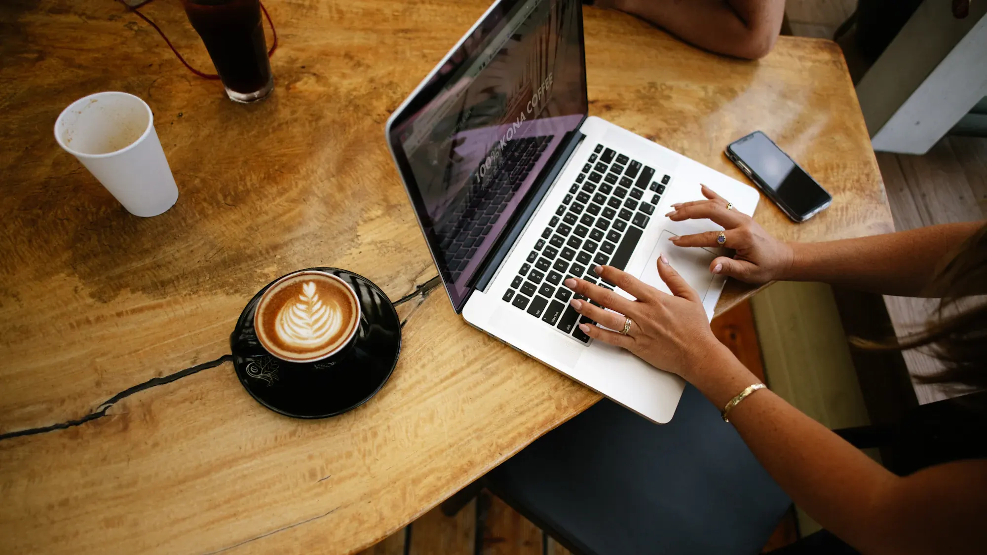 Hands on a laptop beside a coffee on a café table, from above