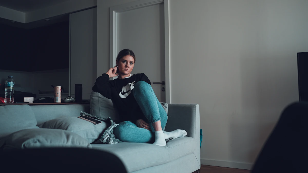 A woman sitting on a grey sofa in a living room, looking at her phone