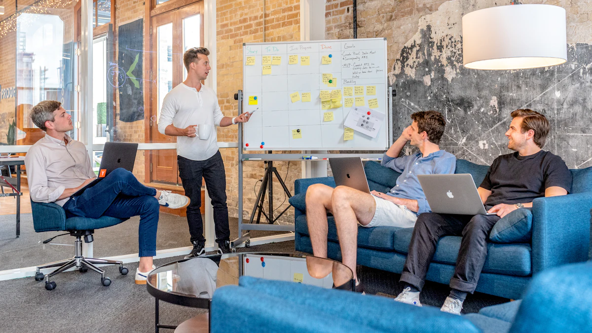 A small team with laptops on sofas listening to a colleague at a whiteboard covered in notes