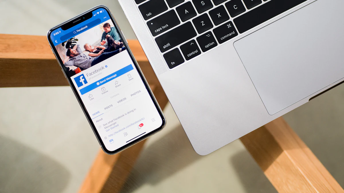An iPhone showing a Facebook page, lying on a desk beside a laptop