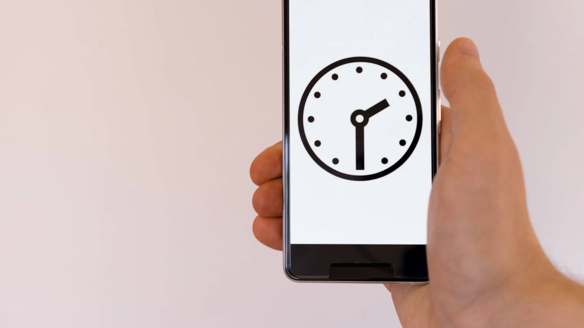 A hand holding a phone that shows a clock face