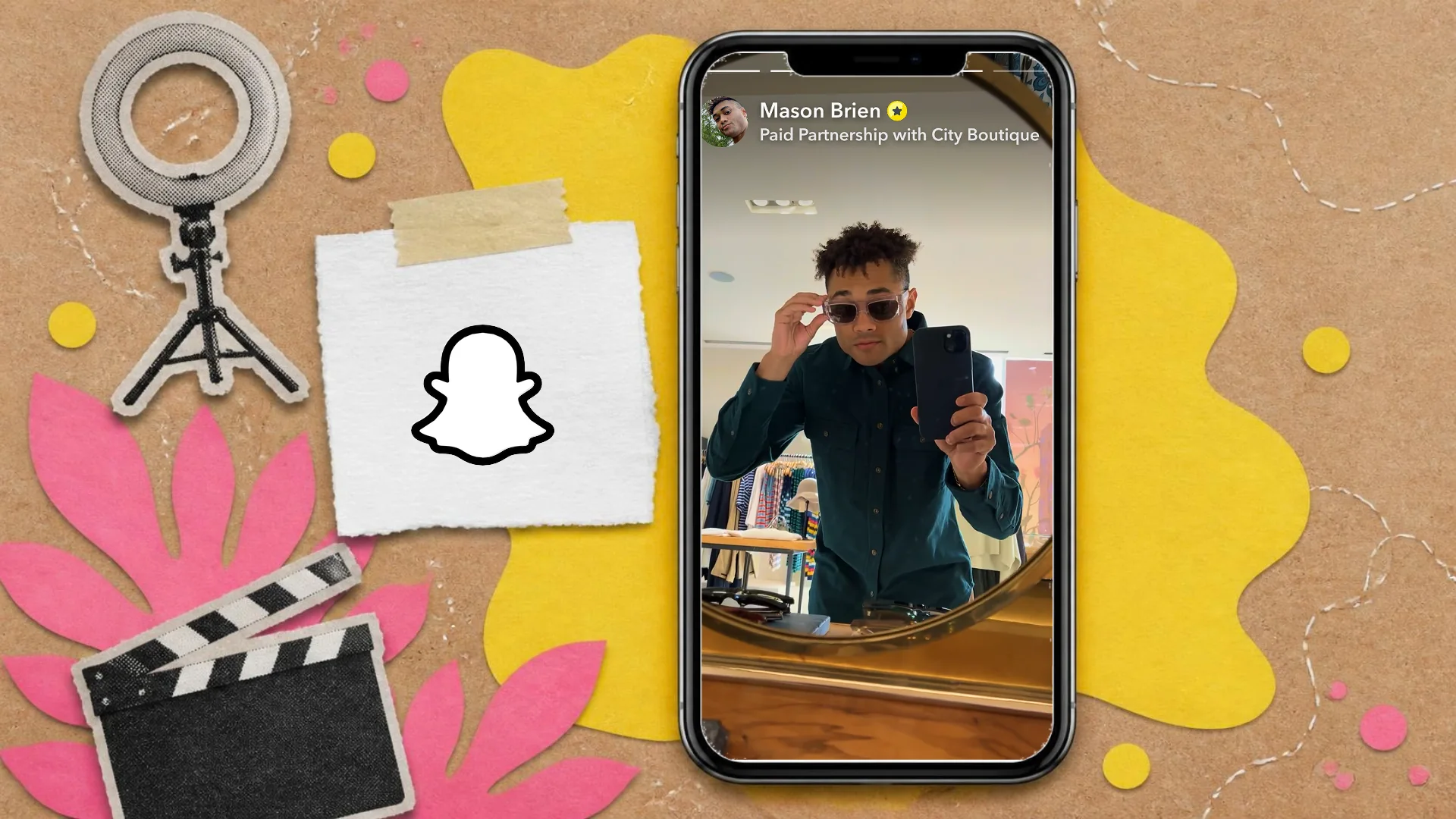 A cut-paper collage on kraft card of a phone showing a Snap labelled as a paid partnership, beside a ring light, a clapperboard and the Snapchat logo on a tag