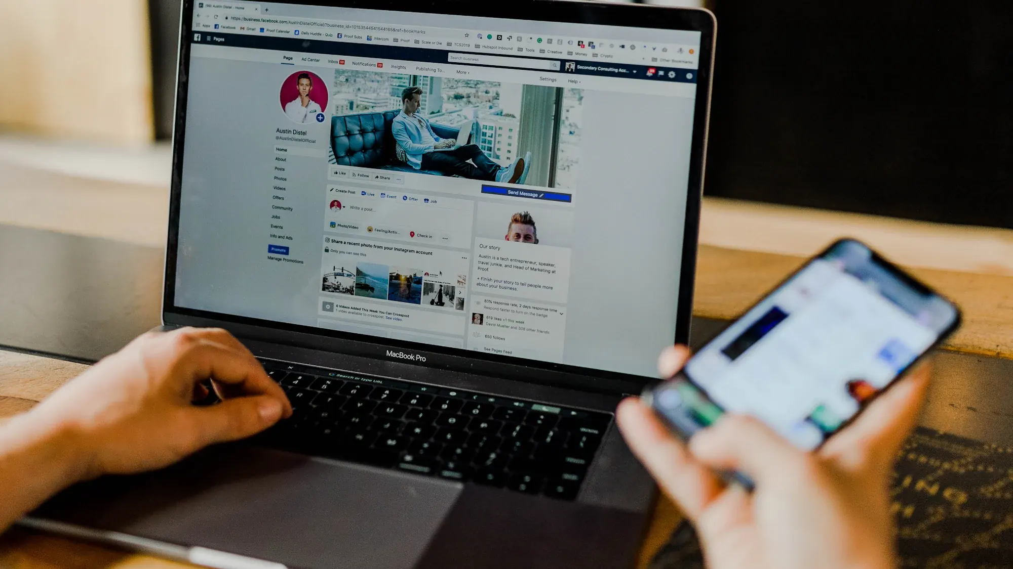 Hands typing on a laptop showing a social media page while holding a phone