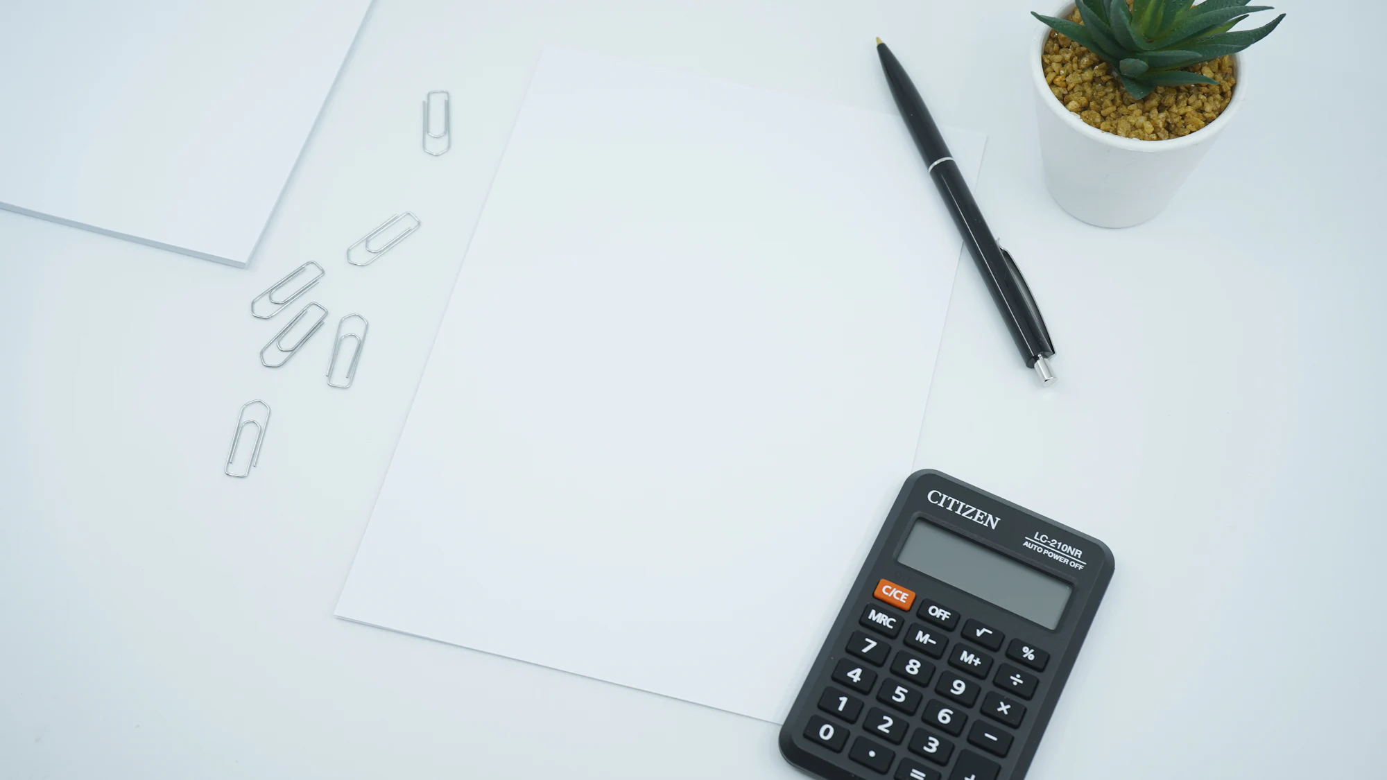 A calculator, a pen and paperwork on a white desk