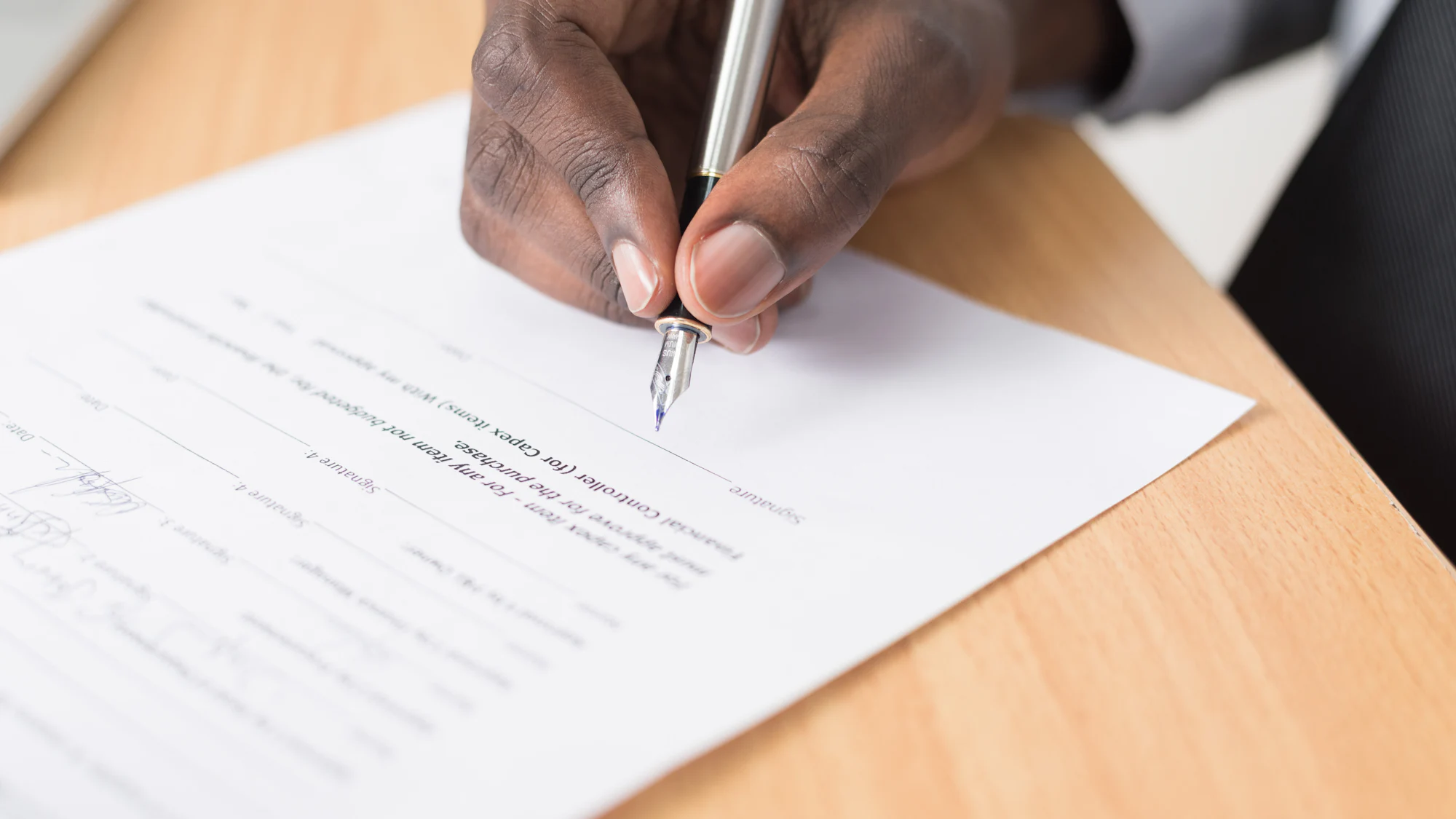 Hands signing a printed document on a wooden desk